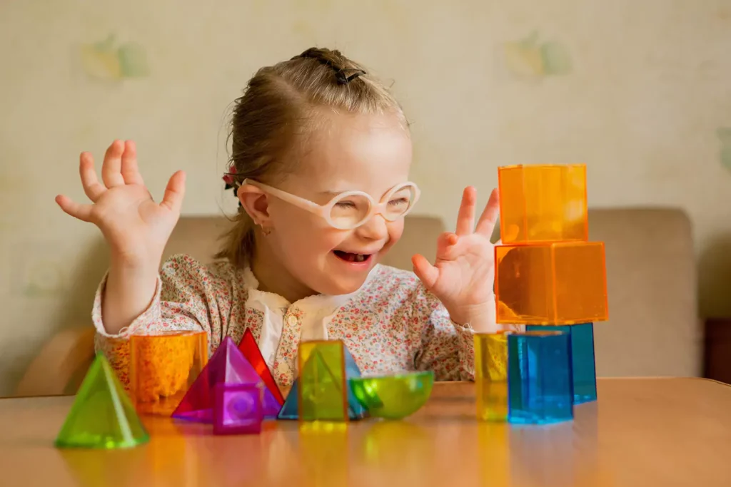 A young girl with down syndrome is smiling while playing with building blocks