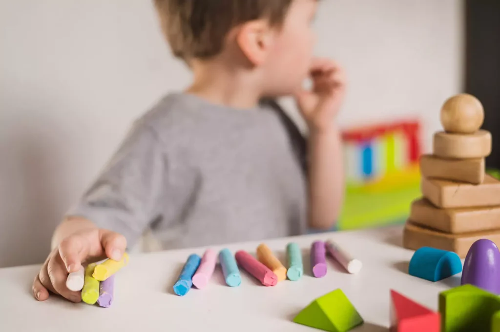 A young boy is holding crayons while engaged in play therapy
